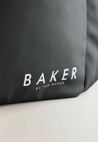 Sac noir en matériau lisse, avec des lettres blanches affichant en évidence "BAKER BY TED BAKER" sur le devant.