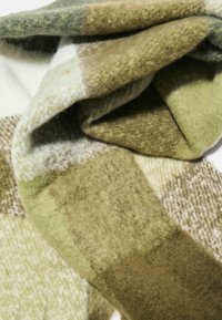 Grøn og beige ternet uldhalstørklæde med blødt, tekstureret stof. Har varierende nuancer af grøn og et ternet mønster gennem hele tørklædet.