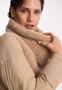 Beżowa kamizelka ocieplana z miękkim, puszystym kołnierzem. Tkanina ma gładką fakturę, a kołnierz kontrastuje z przytulnym, puszystym wyglądem.