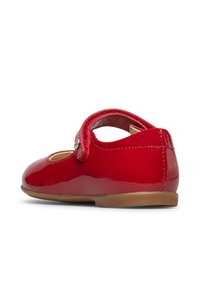 Chaussure Mary Jane en cuir verni rouge avec une sangle Velcro et une semelle plate marron clair, présentée de côté sur un fond blanc.
