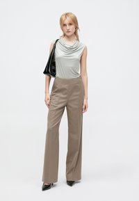 Light gray draped sleeveless top paired with high-waisted beige trousers and black pointed-toe heels, holding a black handbag.