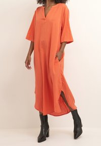 Orange linne maxiklänning med V-ringning, sidospjäll och breda ärmar. Bärs med svarta ankelstövlar och visar upp sin avslappnade silhuett.