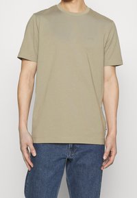 Beige bomulls t-shirt med rundad halsringning och korta ärmar, med en diskret logotyp på bröstet och en avslappnad passform.