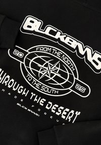 Zwarte sweatshirt met een grote witte grafiek met een wereldbolontwerp en tekst: "BLCK BNNS," "VAN NOORD NAAR ZUID," en "DOOR DE WOESTIJN."