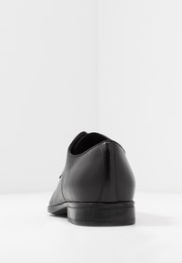 Chaussure habillée en cuir noir au design élégant, bout arrondi, petit talon, texture lisse et détail de couture subtil le long du bord supérieur.