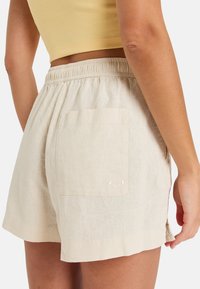 Shorts en lin beige avec une taille élastique, dotés d'une poche arrière et d'un petit logo brodé. Longueur courte avec fentes sur les côtés.