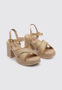 Beige platform sandals with chunky block heels, woven front straps, and adjustable ankle strap featuring a metallic buckle detail.