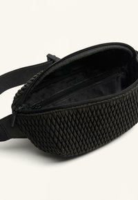 Trendy fanny pack țesut, de culoare neagră, cu un exterior texturat și un interior neted. Include un compartiment cu fermoar și o curea ajustabilă.