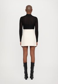 Zwart gestreepte lange mouwen top, witte minirok en kniehoge zwarte haklaarzen, gezien van achteren op een neutrale achtergrond.