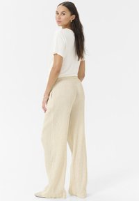 Pantalon wide-leg beige clair en tissu texturé, associé à un t-shirt crème à manches courtes. Design simple avec une coupe décontractée.