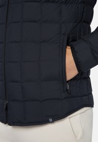 Marinblå puffjacka med kviltat mönster, med framförande dragkedja och sidoficka. Mjuk textur och elastiska ärmslut för värme.