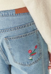 Jeans in denim blu chiaro con una tasca posteriore decorata da ricami floreali rossi e bianchi. Etichetta in pelle sulla vita. Tessuto morbido.