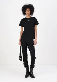 Black t-shirt with a round logo on the chest, paired with black joggers featuring white side stripes, and black knee-high boots.