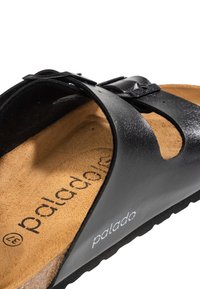 Svart lädersandal med ett texturerat rem, justerbar spänne och en korkfotbädd; har en tryckt logotyp och en hållbar gummisula.