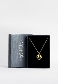 Guldtonad halsband med en knuten hänge, visas i en svart sammetfodrad låda, med en texturerad metallisk yta och varumärkeslogotyp.