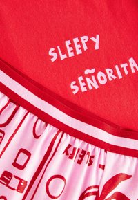Red fabric with white text stating "SLEEPY SEÑORITA," featuring a gathered pink skirt with red graphic patterns. Soft texture, casual design.