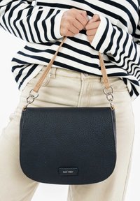 Black pebbled leather handbag with a long tan strap, curved shape, and metal hardware. Brand label visible on front.