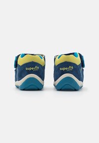 Lasten siniset mokka-tennarit keltaisilla verkkoaksentilla, joissa on tarranauha ja erottuvat valkoiset ja siniset pohjat. "superfit"-logo näkyvissä.