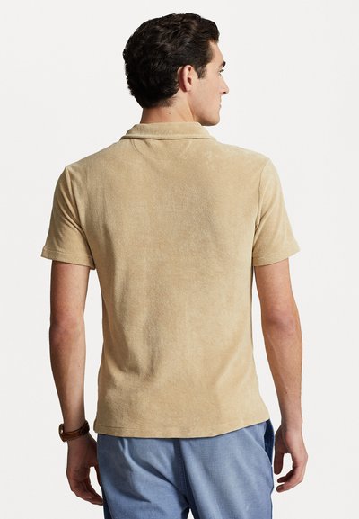 Polo à manches courtes avec col en tissu éponge beige, présentant une texture douce. Le dos présente un design simple et ajusté.