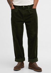 Σκούρο πράσινο παντελόνι καμπάνα με ίσια γραμμή, διαθέτει κλείσιμο με κουμπί, δύο μπροστινές τσέπες και γυρισμένα μπατζάκια.