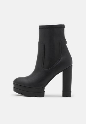 Bottine noire à talon haut avec une semelle plateforme épaisse et une finition en cuir lisse, vue de profil sur un fond uni.