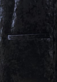 Indumento in velluto nero caratterizzato da una morbida texture, un design elegante e una piccola tasca piatta integrata nel tessuto.