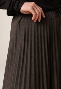 Plisserad mörkgrå kjol med ett strukturerat tyg och elastisk midjeresår, med vertikala ränder och en slät yta.