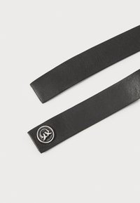 Curea din piele neagră cu o textură netedă. Caracteristică un accent metalic circular cu un design. Capetele sunt tăiate drepte.