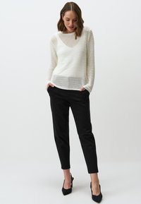 Witte, gebreide trui met een gestructureerde, open weving; ronde hals en lange mouwen. Gecombineerd met zwarte, tapered broek en zwarte hakken.