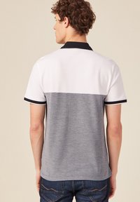 Camisa polo de manga corta con un diseño de bloques de color, con la mitad superior blanca y la mitad inferior gris, complementada por un cuello y bordes negros.