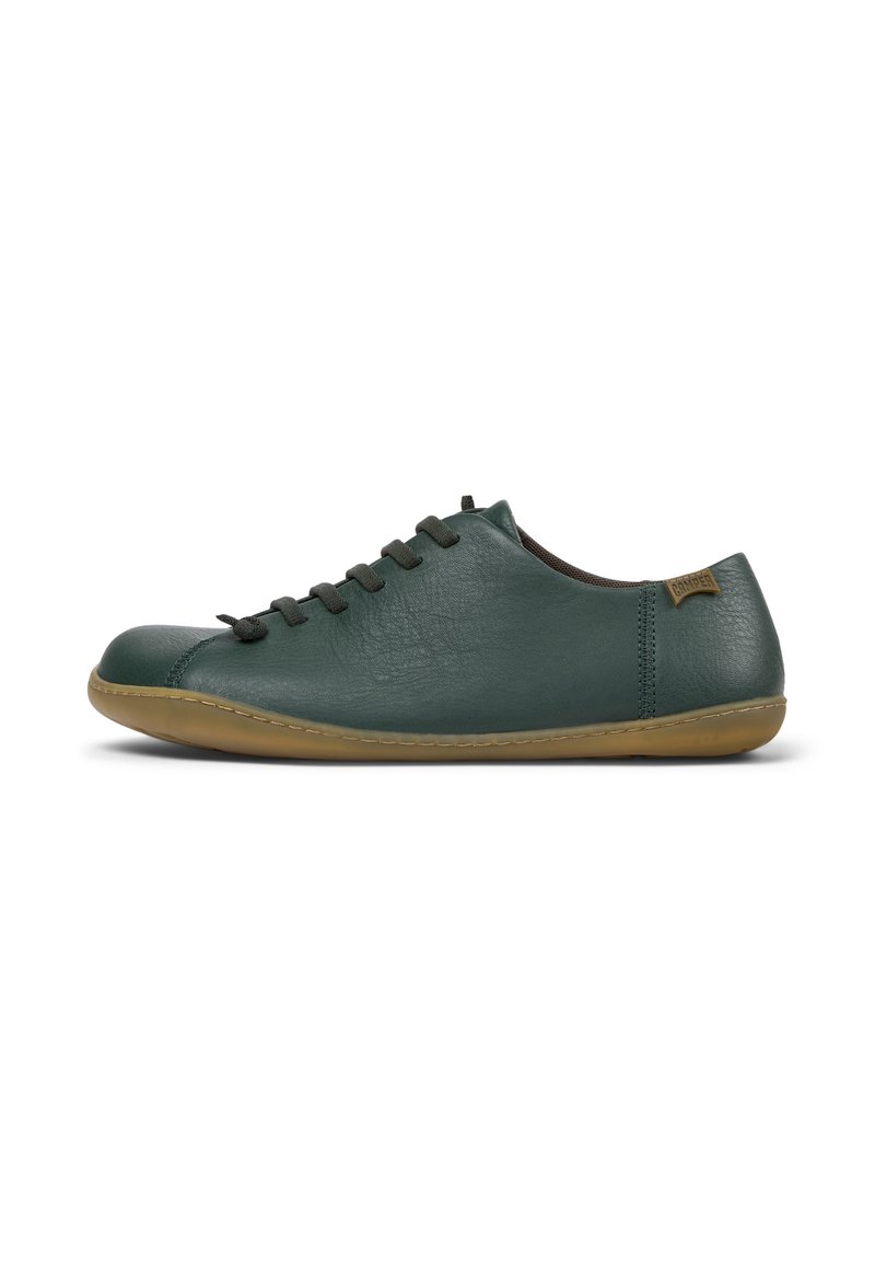 Zapato de cuero verde con punta redondeada, cinco ojetes y cordones marrones. Presenta una suela de goma flexible y un pequeño logo en el talón.