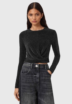 Zwarte langekleurige top met een twist-voorkant ontwerp, gemaakt van een gestructureerd, sprankelend materiaal. Gecombineerd met hoge taille donkerdenim jeans.