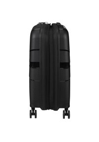 Musta kova matkalaukku teksturoidulla pinnalla, kaksipistoke ja neljä pyörivää pyörää liikkuvuuteen. Kompakti suorakulmainen muotoilu.