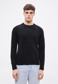 Μαύρο πουλόβερ με στρογγυλή λαιμόκοψη, κατασκευασμένο από απαλό ύφασμα, με μακριά μανίκια και ριμπ τελείωμα. Συνδυάζεται με τζιν παντελόνι σε ανοιχτό μπλε χρώμα.