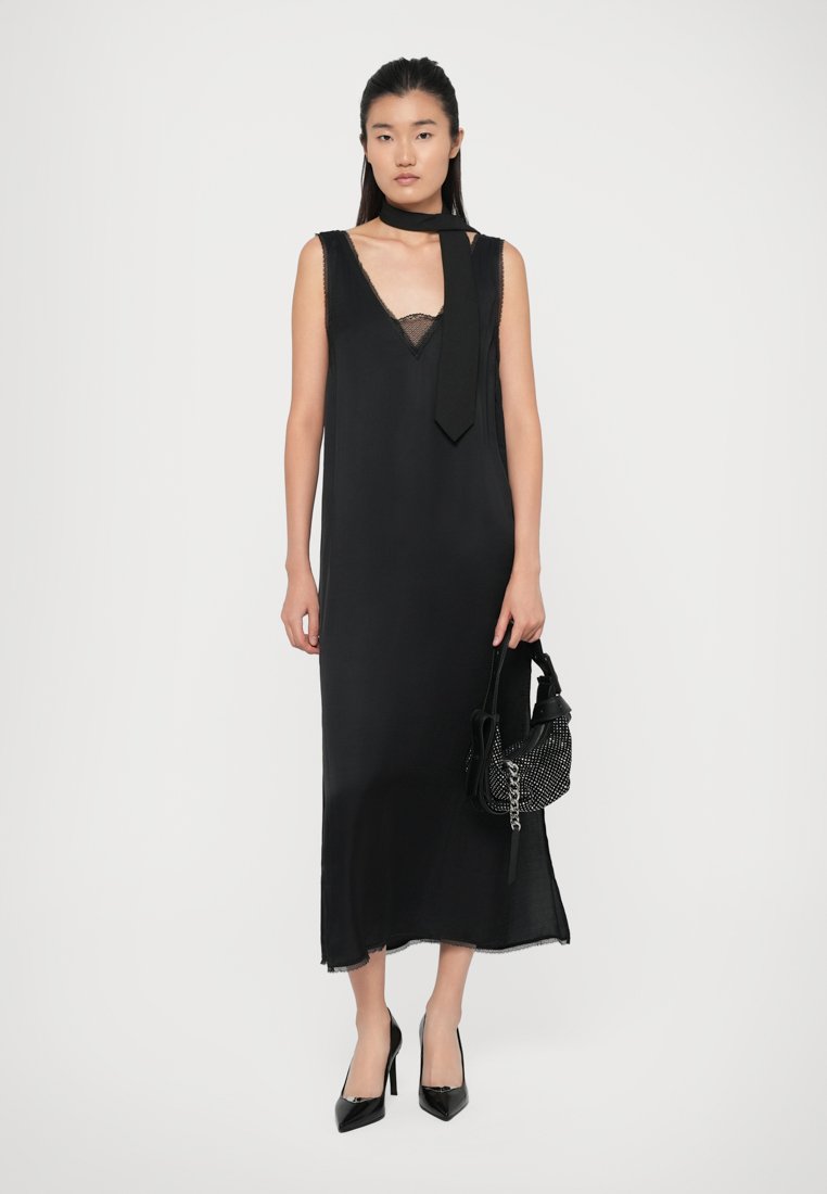 Robe noire sans manches avec un décolleté en V et une bordure en dentelle. Tissu léger, longueur cheville, avec une texture soyeuse. Assortie à un sac à perles et des talons hauts.