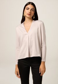 Top a maniche lunghe rosa chiaro con scollatura a V e dettagli di pieghe sottili. Abbinato a pantaloni neri, con tessuto liscio e vestibilità rilassata.