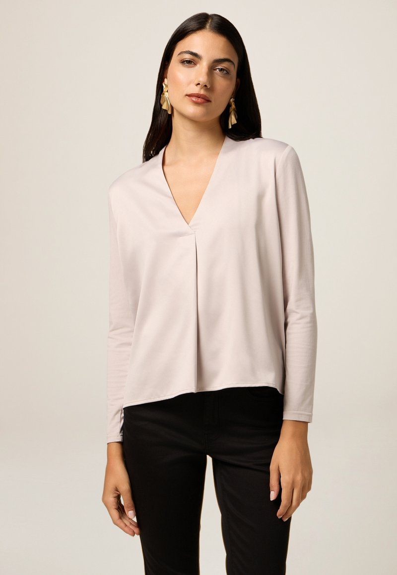 Top a maniche lunghe rosa chiaro con scollatura a V e dettagli di pieghe sottili. Abbinato a pantaloni neri, con tessuto liscio e vestibilità rilassata.