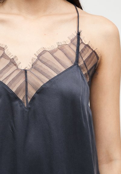 Κοντινό πλάνο ενός ατόμου που φοράει μια σκοτεινή μεταξωτή καμησόλα με λεπτές τιράντες και ραμμένη διάφανη δαντέλα με βολάν κατά μήκος του λαιμού.