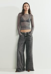 Prosojen dolg rokav sive barve z nežnimi pikicami, kombiniran z visokim pasom, širokimi črnimi kavbojkami z bledenim vzorcem in kontrastnim šivom.