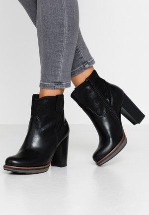 Bottes noires à la cheville en cuir lisse et en daim, avec une fermeture éclaire sur le côté et un talon carré texturé.