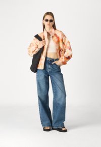 Spalvinga, laisvos kirpimo striukė su abstrakčiu raštu oranžinės ir rožinės spalvos, derinama su aukštu liemeniu, plačiomis mėlynomis džinsinėmis kelnėmis ir juodomis šlepetėmis.