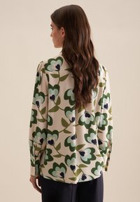 Camicia a maniche lunghe realizzata in tessuto leggero, caratterizzata da una stampa floreale in diverse tonalità di verde e blu su uno sfondo beige. Fit rilassato con polsini a bottoni.