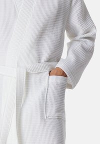 Accappatoio bianco in tessuto waffle con cintura, maniche lunghe e due tasche laterali, che offre una vestibilità comoda e rilassata.