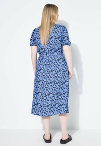 Vestido de estampado de leopardo azul con mangas cortas abullonadas, cintura ceñida y falda fluida. Tejido suave, de longitud media, combinado con sandalias negras.