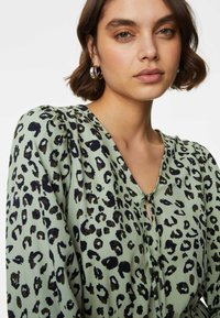 Leopardprint blouse in lichtgroen, met een V-hals, keyhole detail en geraffineerde schouders, gemaakt van textuurstof.