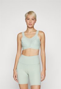Lys grønn sports-bh med brede stropper, rynkede detaljer og en glatt tekstur, kombinert med matchende høyt midje shorts.