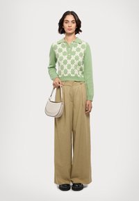 Grøn strikket sweater med et mønstret front, beige vide bukser og en lille håndtaske. Sweateren har knapper og ribbede ærmer.