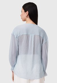 Helles blaues Blusenshirt mit gerunzelter Textur und transparentem Oberteil. Verfügt über lange Ärmel mit elastischen Bündchen und einem runden Halsausschnitt.