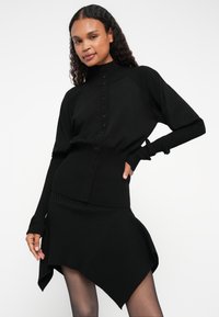 Černý žebrovaný pletený svetr s vysokým límcem a zapínáním na knoflíky. Svetr má tříčtvrteční rukávy a asymetrický design sukně.