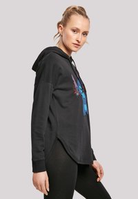Svart hettegenser med løs passform, kenguru-lomme og fargerik Stitch-grafikk. Lange ermer med ribbestrikkede mansjetter og sidesplitter. Myk stoffkvalitet.